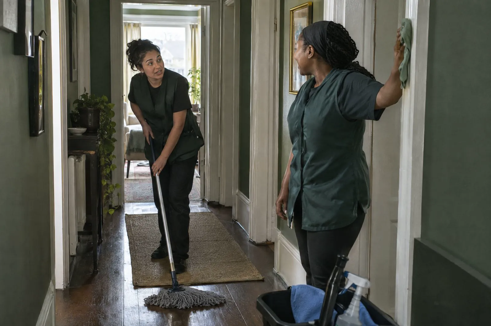 Two cleaners working together in the hallway of a home